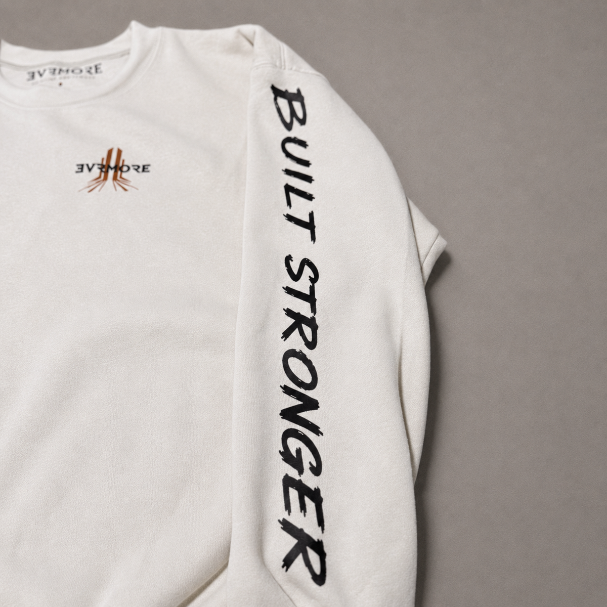 An off-white long-sleeve sweatshirt with 'BUILT STRONGER' printed vertically in black on the right sleeve and a small black and orange logo on the left chest, shown on a neutral gray background.