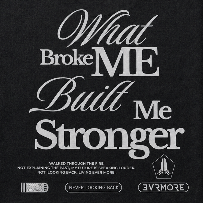 A black crewneck t-shirt with a white graphic text print reading 'What Broke ME Built Me Stronger' and smaller text below, displayed flat against a textured gray background.