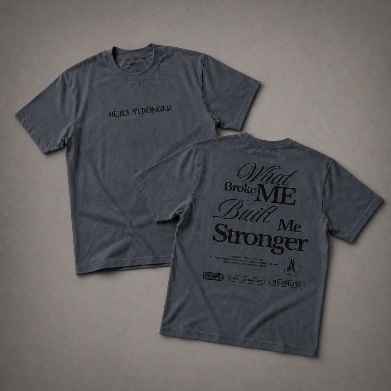 Two views of a dark gray graphic t-shirt on a textured gray background. The front view shows 'BUILT STRONGER' printed in black on the chest, and the back view shows a large black graphic reading 'What Broke Me Built Me Stronger' with smaller text and logos below.