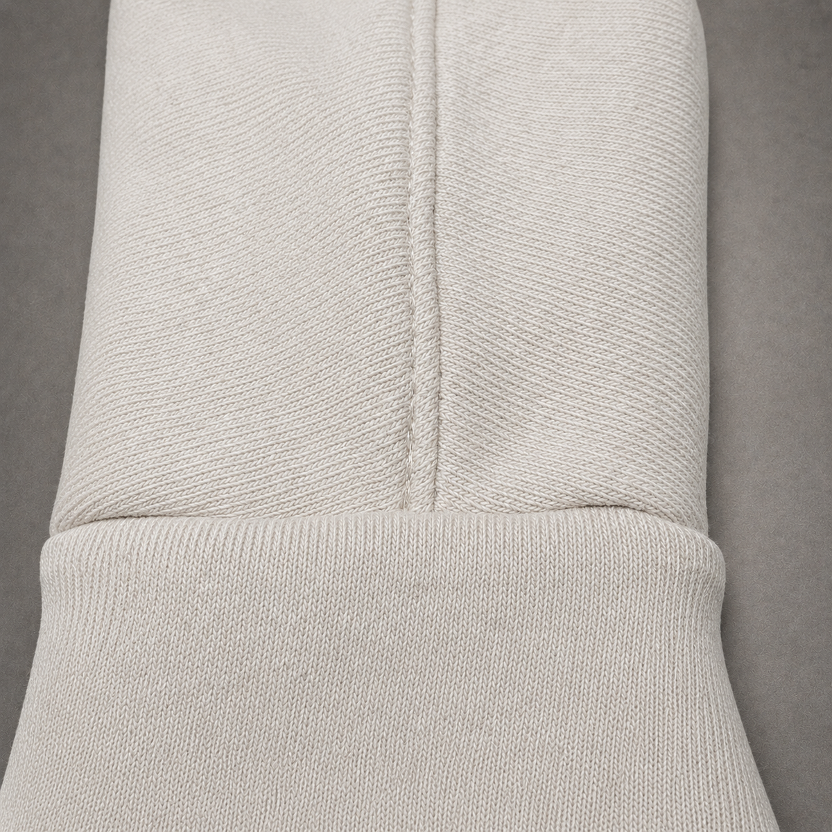 Close-up of a light beige ribbed knit fabric, showing the texture and a central seam, set against a neutral gray background.