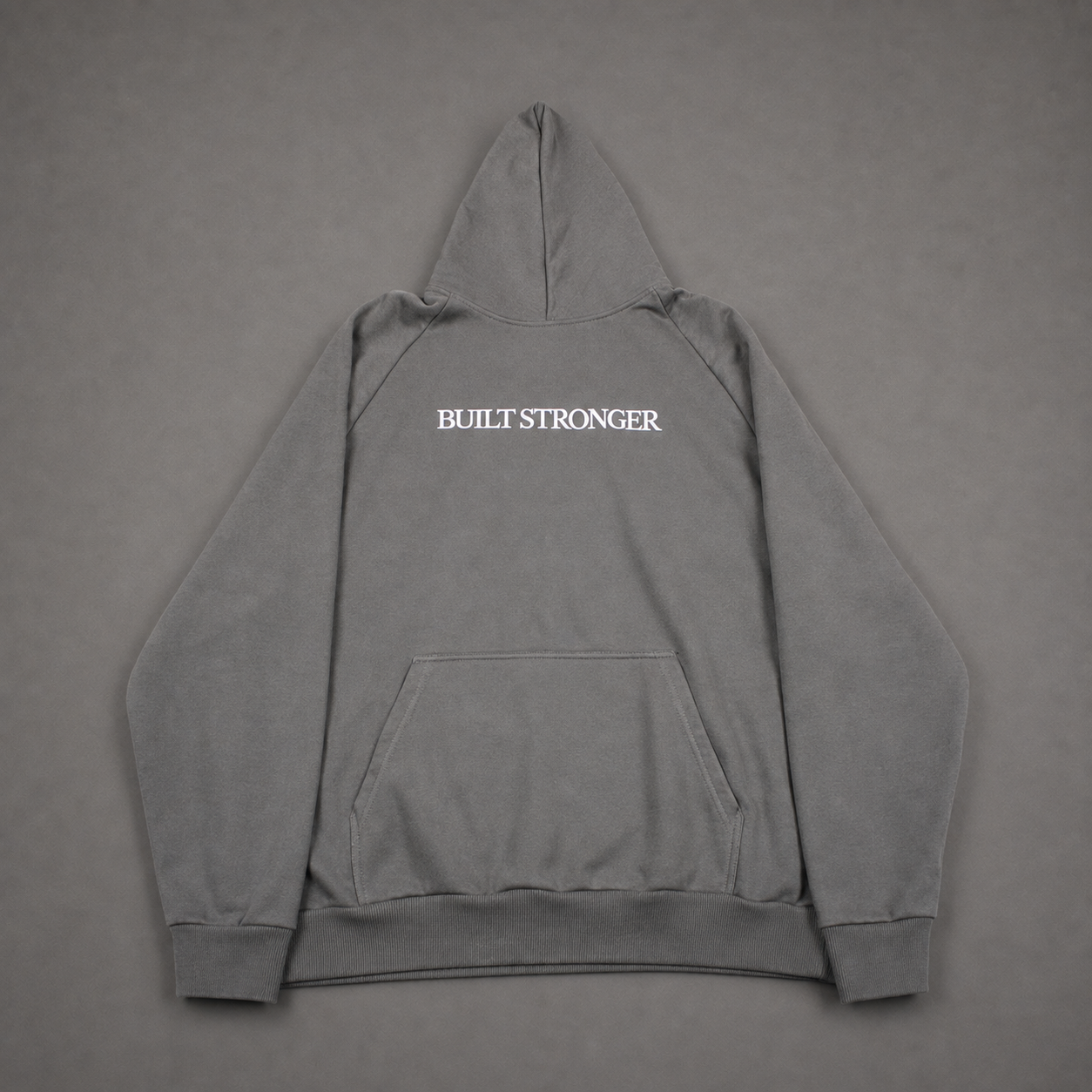 A gray pullover hoodie shown from the back, featuring the words 'BUILT STRONGER' printed in white capital letters across the upper back, laid flat against a matching gray background.