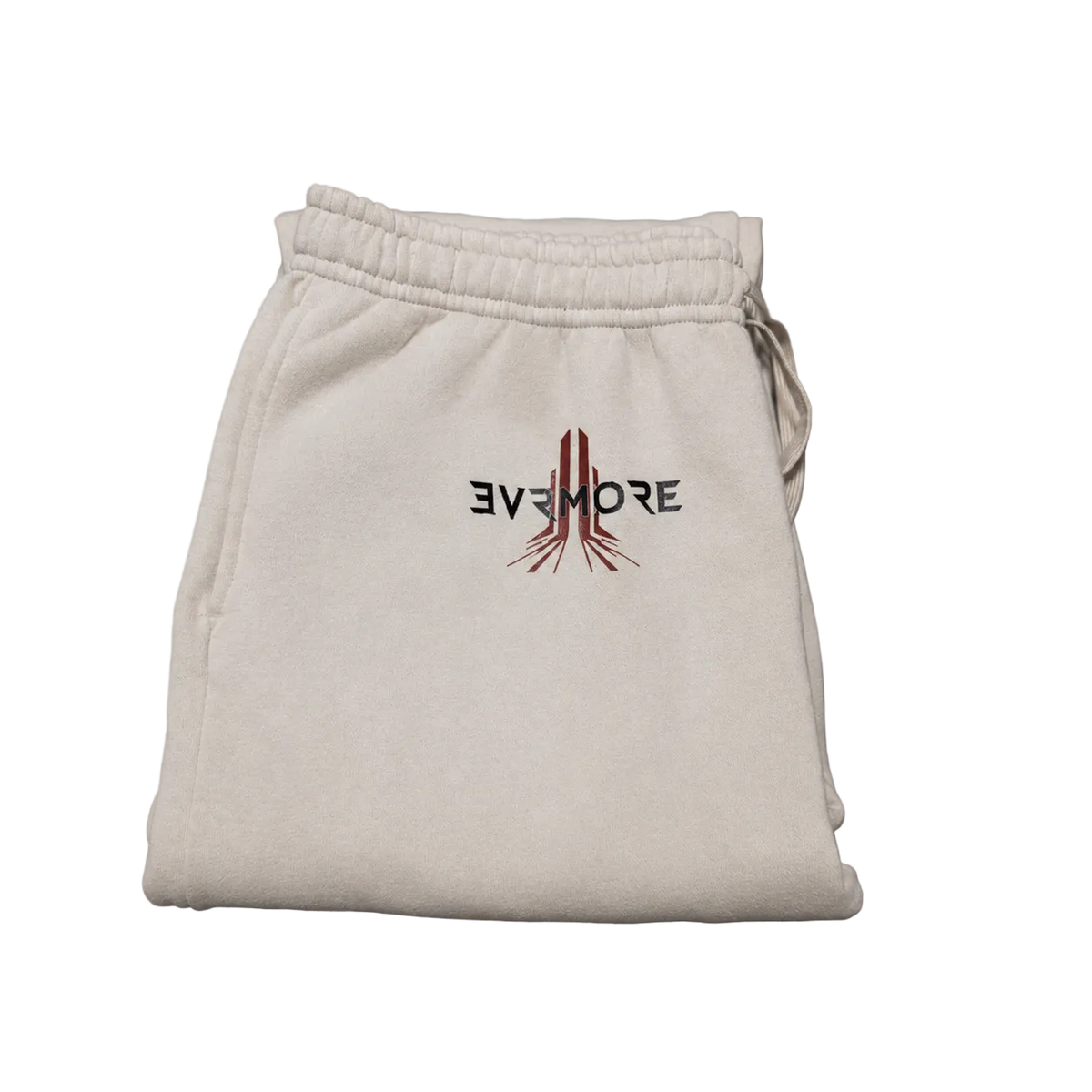 A folded pair of off-white sweatpants with a drawstring waistband, featuring a black and red embroidered logo on the front that reads 'EVJEMORE' with a stylized vertical graphic, set against a solid gray background.