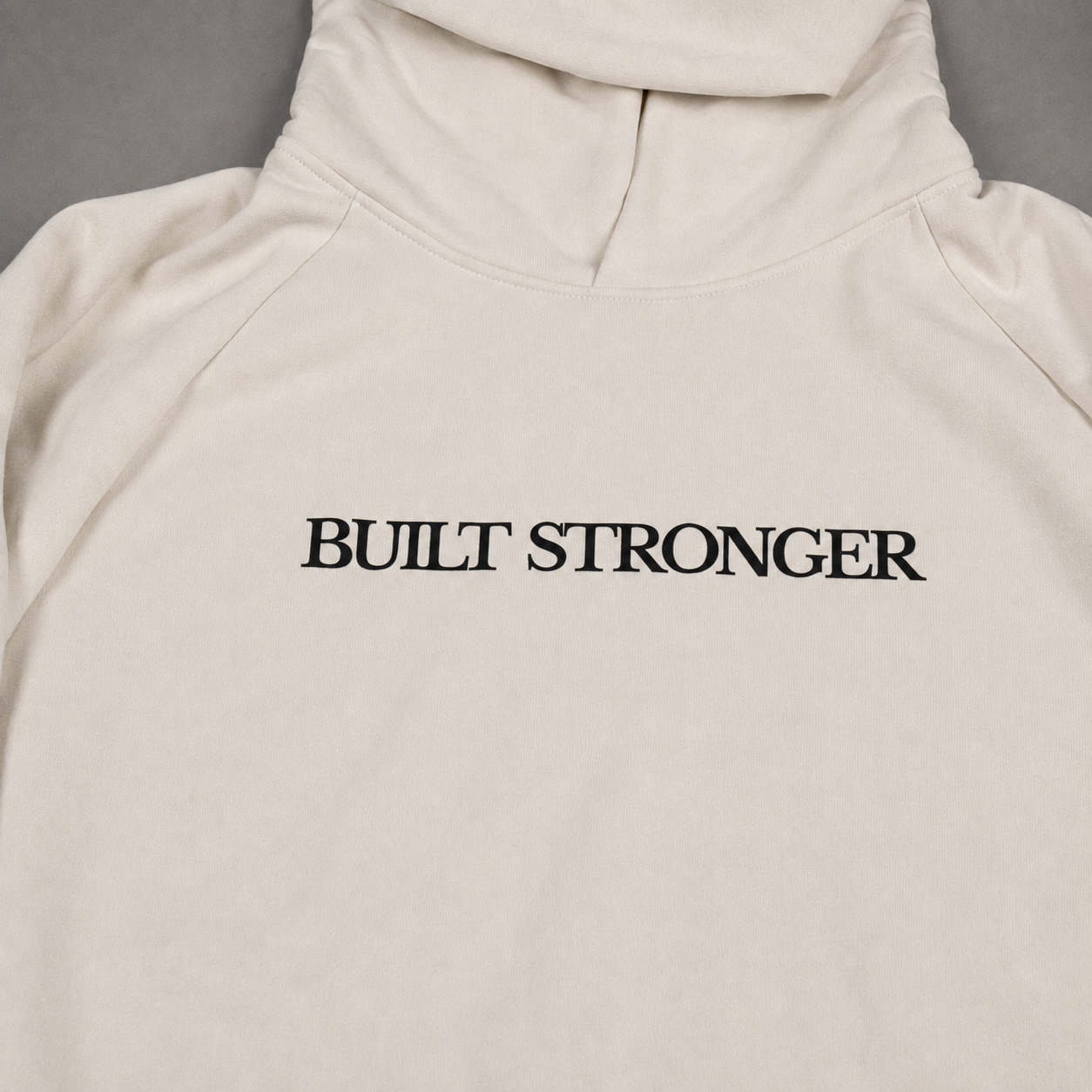 An off-white hooded sweatshirt with the words 'BUILT STRONGER' printed in black serif lettering across the chest, laid flat against a neutral gray background.