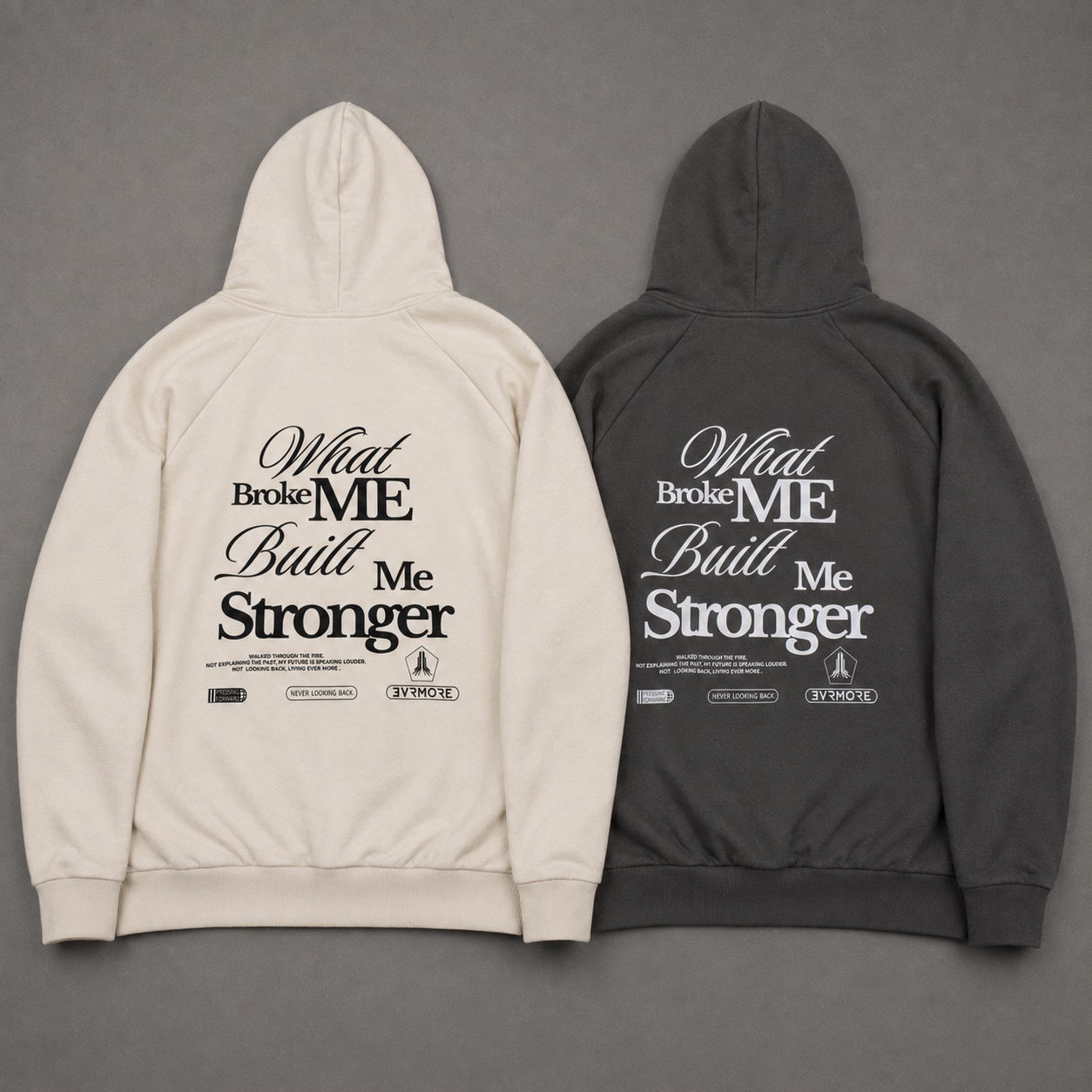 Two hooded sweatshirts shown from the back on a gray background, one in off-white and one in dark charcoal gray. Both feature a large typographic graphic on the back reading 'What Broke ME Built Me Stronger' in black and white lettering.