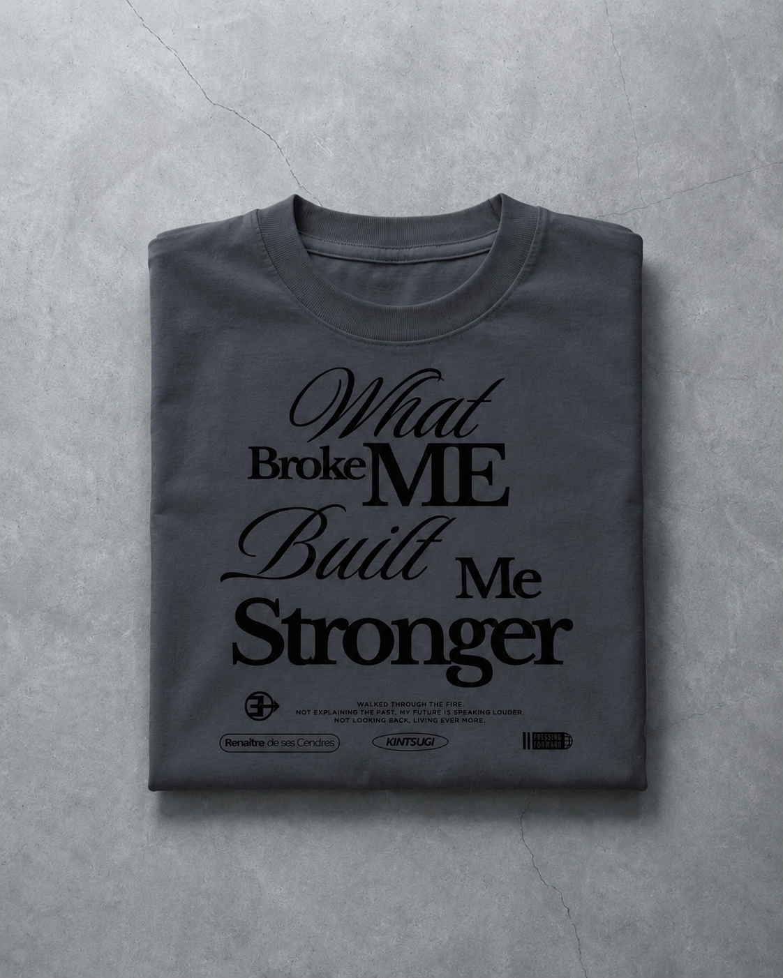 Folded gray t-shirt with 'What Broke Me Built Me Stronger' text on a textured gray surface
