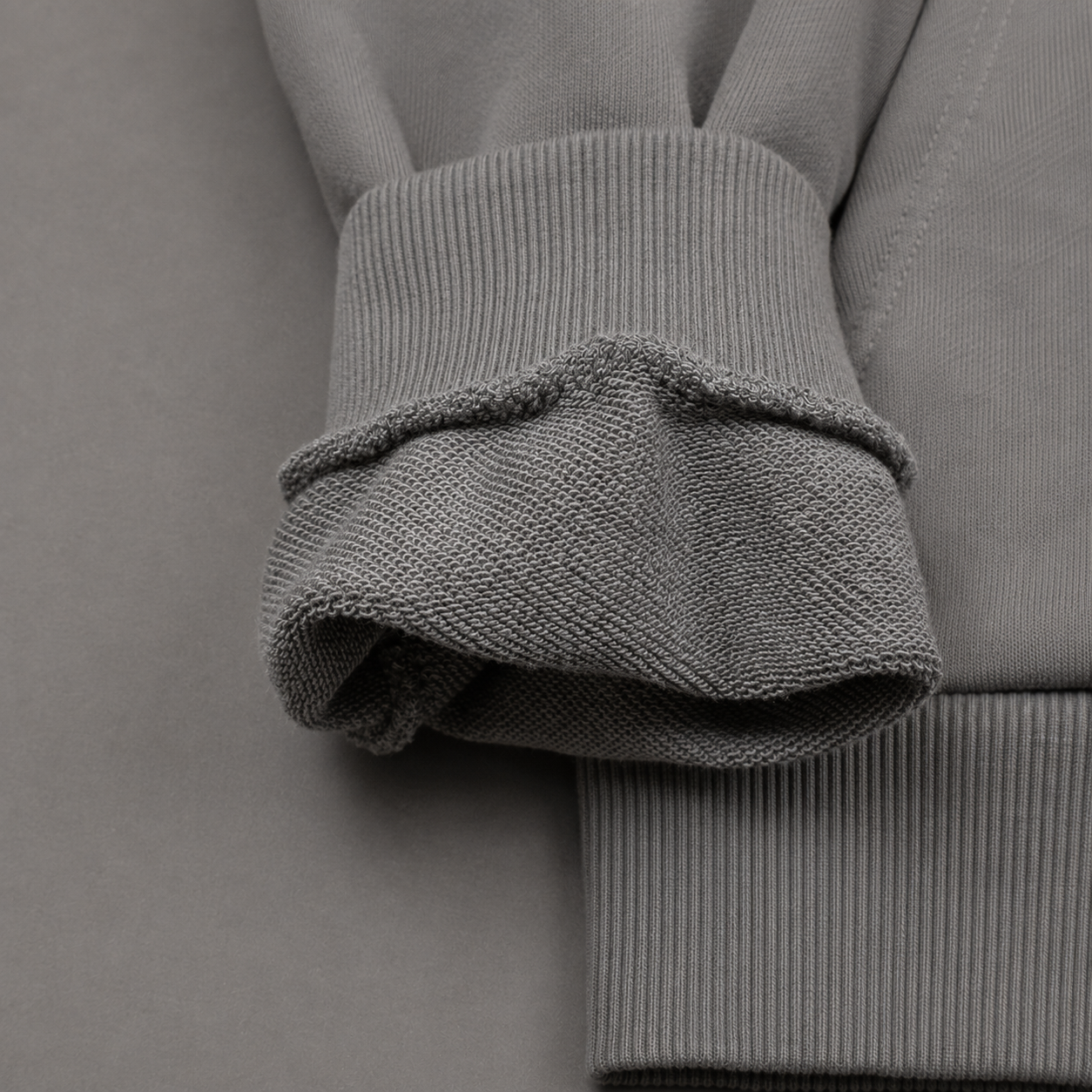 Close-up of a gray ribbed knit garment detail, showing the folded cuff and ribbed sleeve construction.