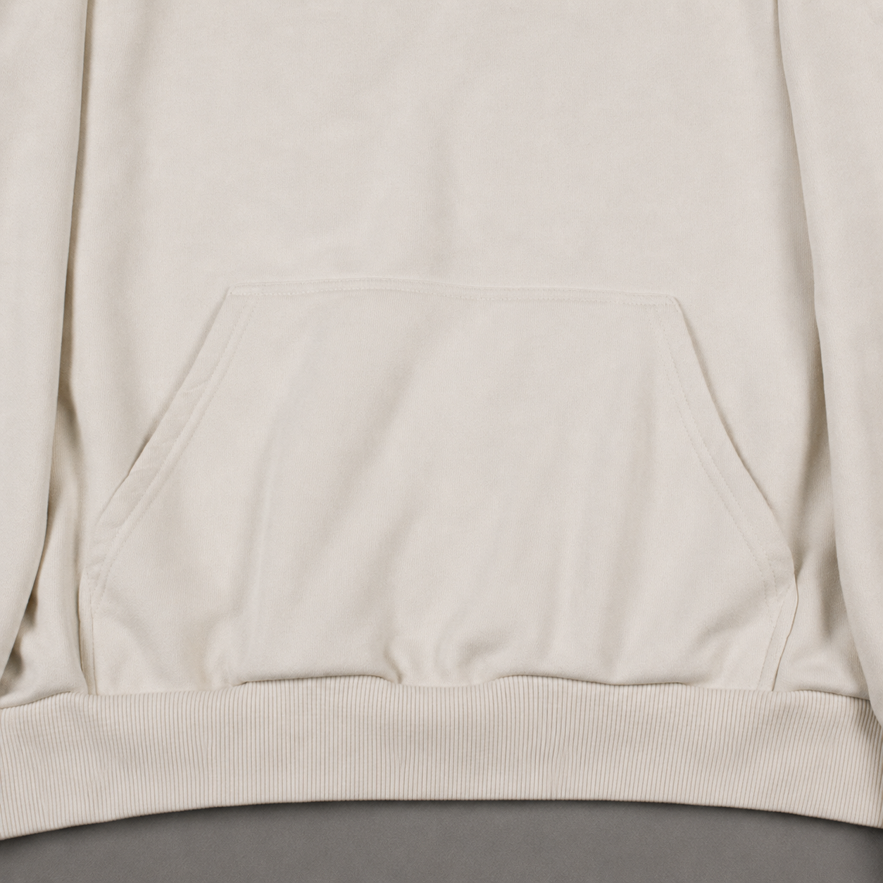 Close-up of a light cream or off-white sweatshirt showing the front kangaroo pocket and ribbed hem.