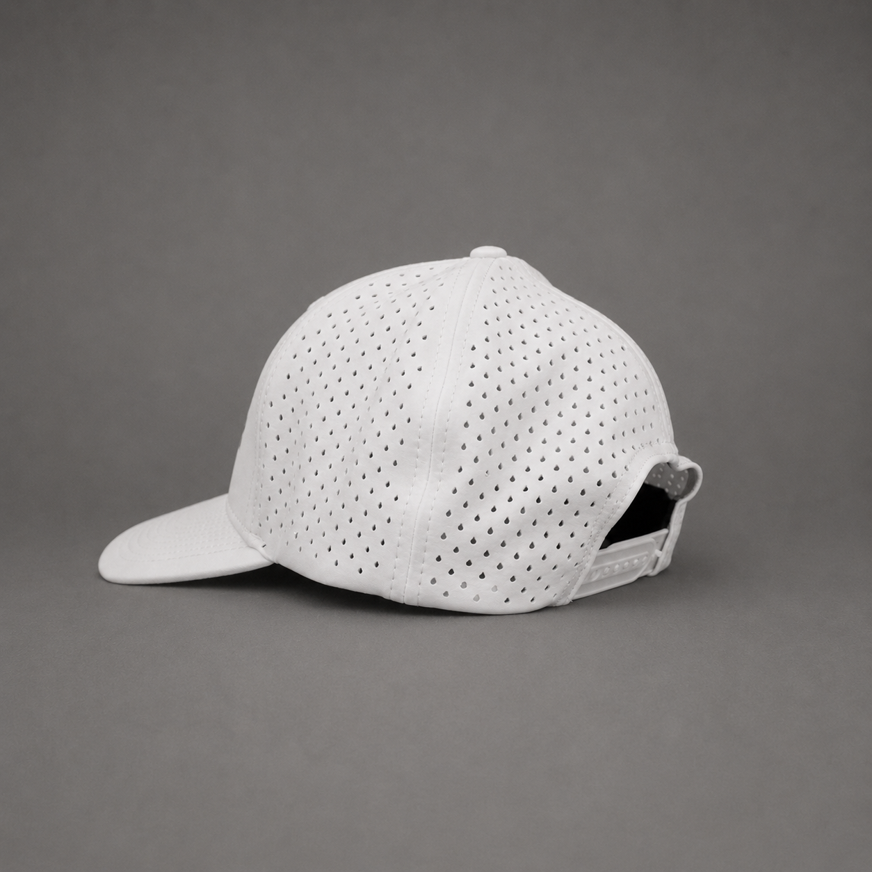 A white baseball cap with a perforated mesh pattern on the front panels and a curved brim, shown from a three-quarters angle against a solid gray background.