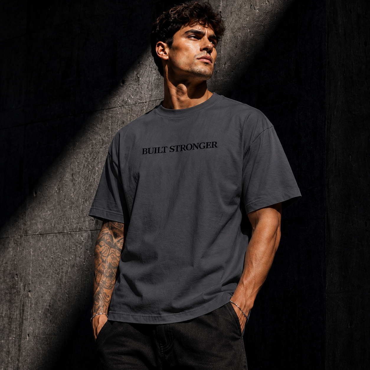 Man wearing a gray t-shirt with 'BUILT STRONGER' text against a dark background