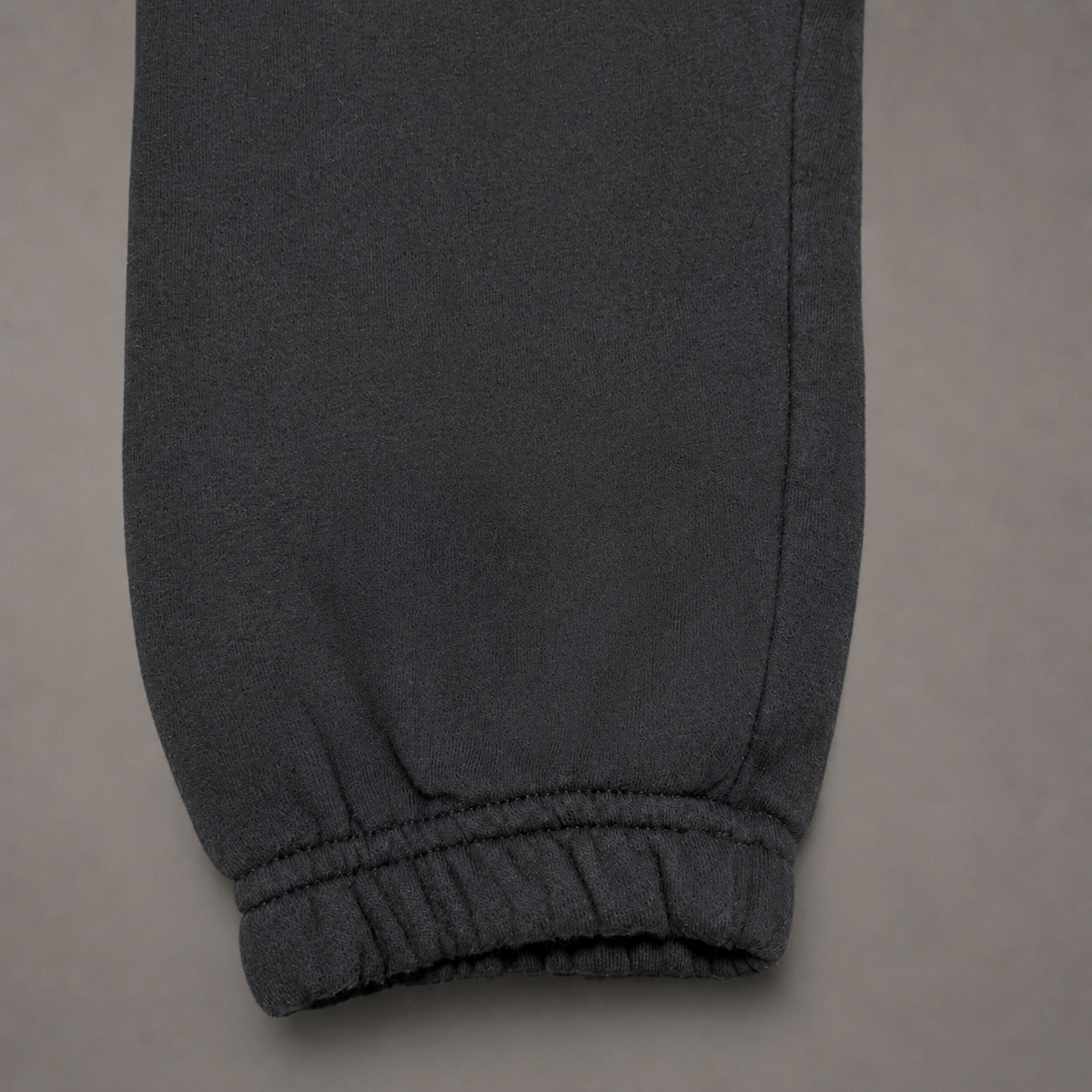 Close-up of a dark gray sweatpants leg showing the ribbed elastic cuff, set against a neutral gray background.